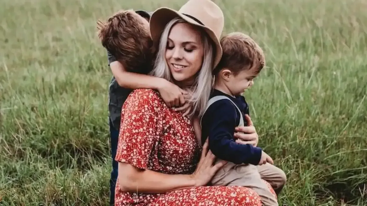 A woman is sitting in the grass with two children.
