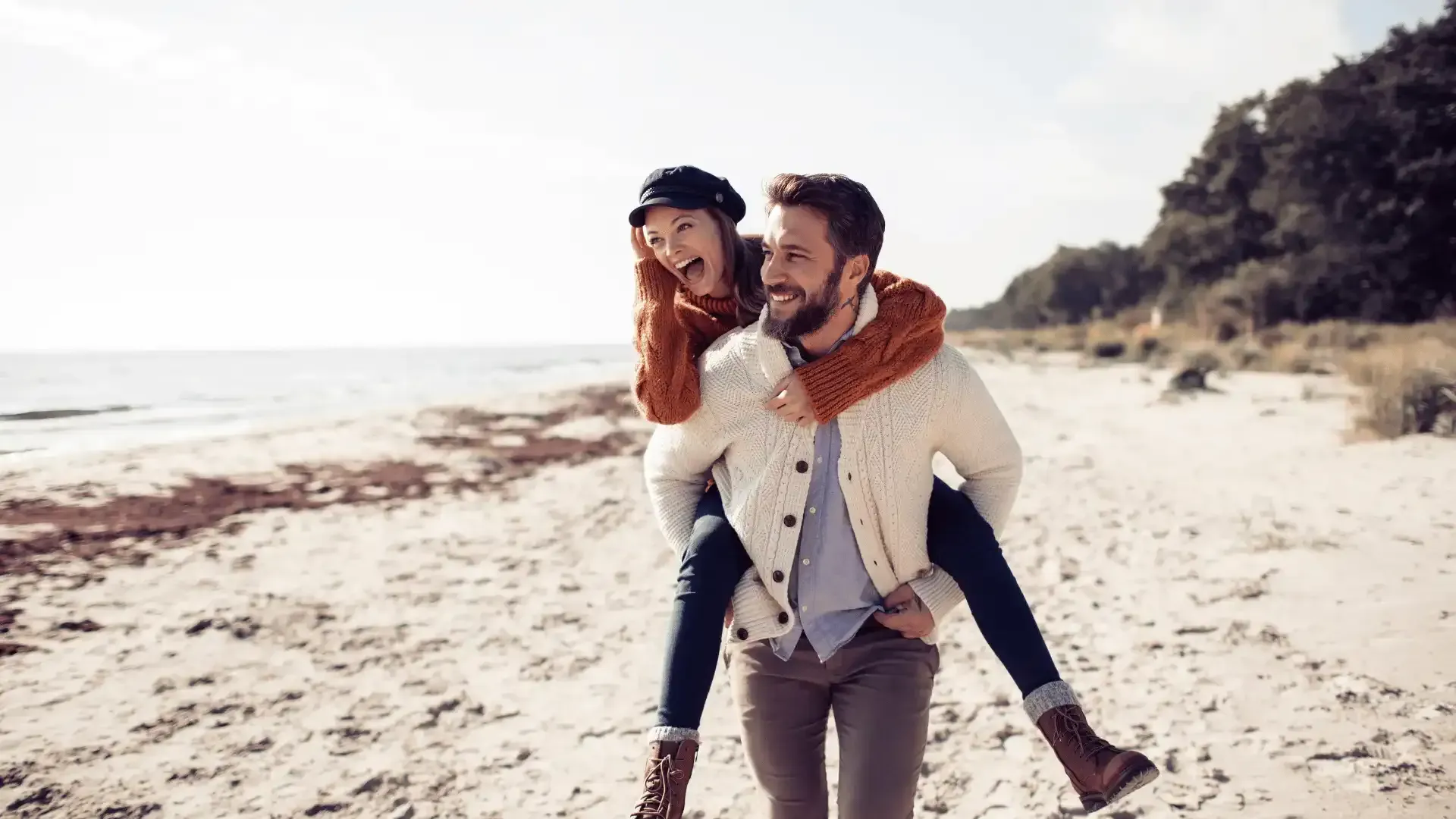 A man is carrying a woman on his shoulders on the beach.