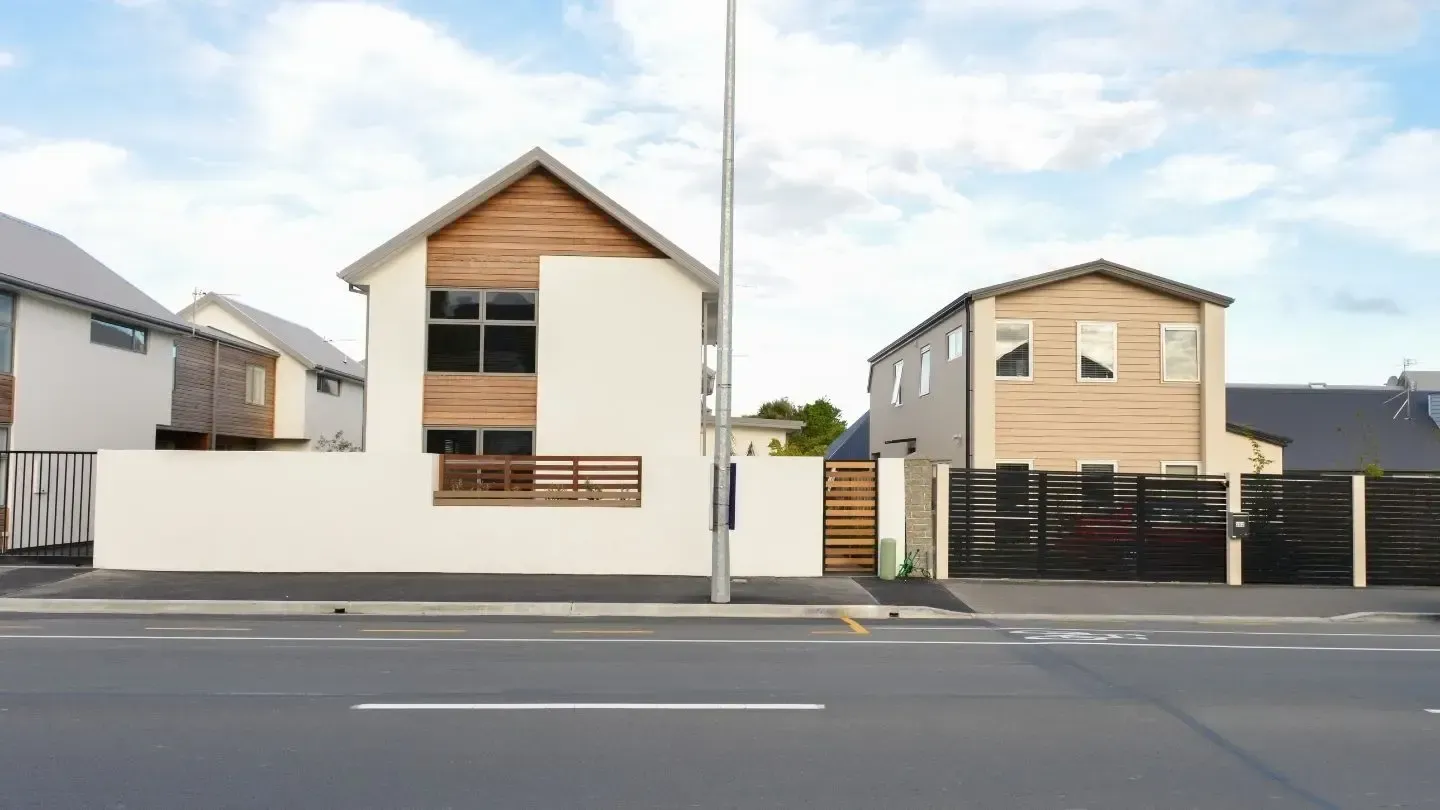 Two-story modern homes with light wood accents and white walls near a street with a tall pole.