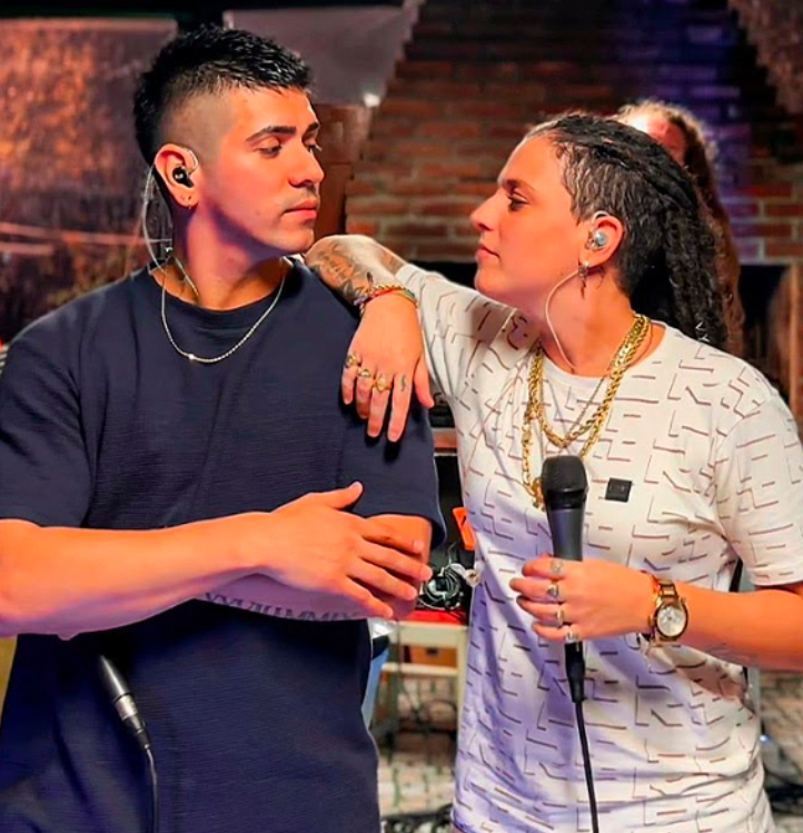 Dos músicos en el escenario, uno sosteniendo un micrófono y mirando al otro durante una actuación.