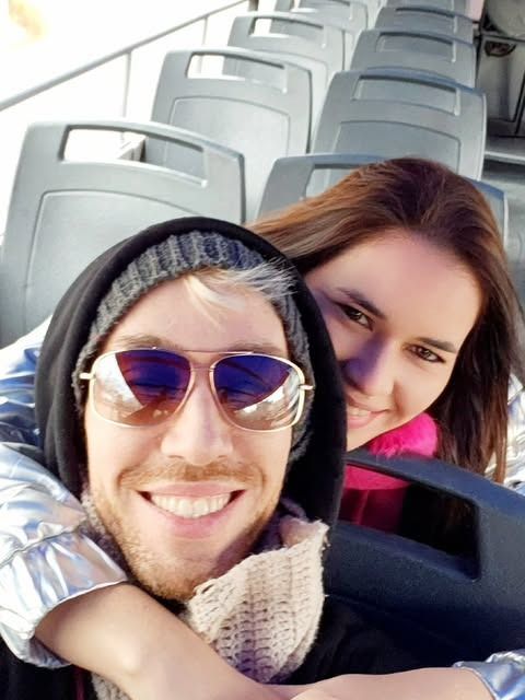 Dos personas sonrientes se toman una selfie en un autobús, con filas de asientos vacíos detrás de ellas.