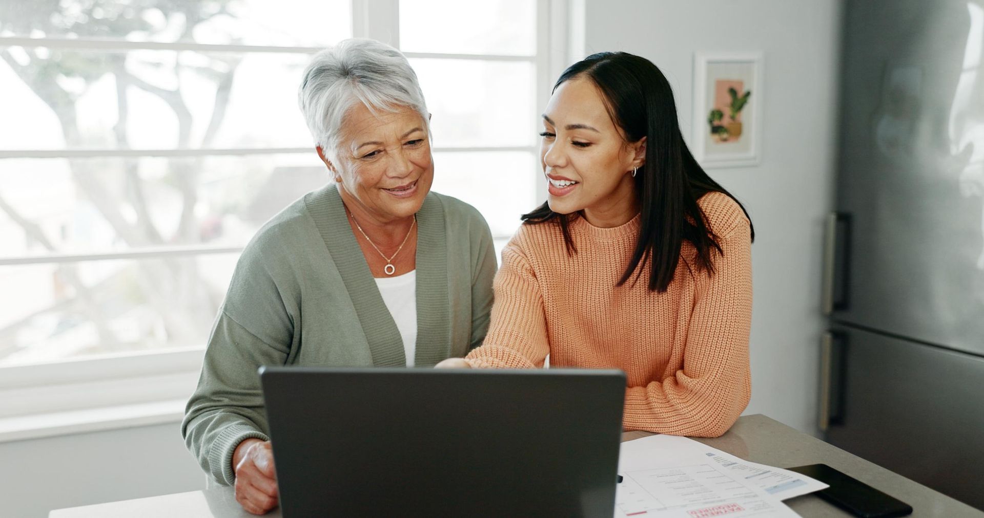Two women are sitting at a table looking at a laptop computer.
