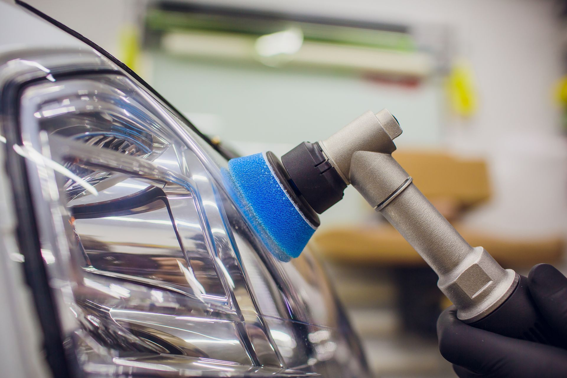 Headlight being polished with a blue buffer by a gloved hand.