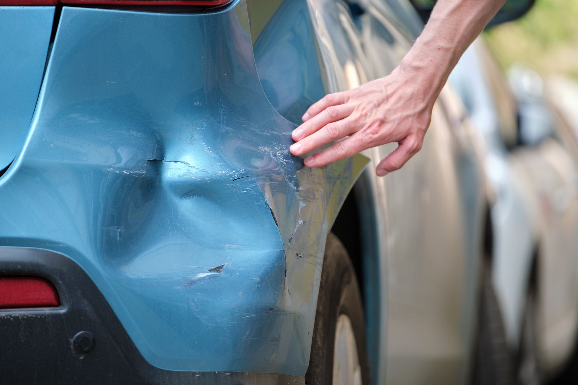 Hand touching a dented, blue car bumper after a collision.