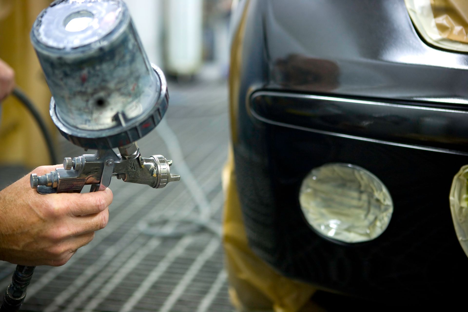A person spray-painting a black car bumper in a workshop.