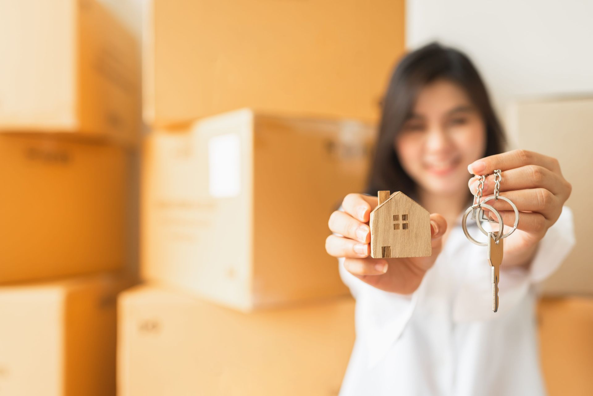 Woman holding house-shaped keychain and keys in front of stacked moving boxes