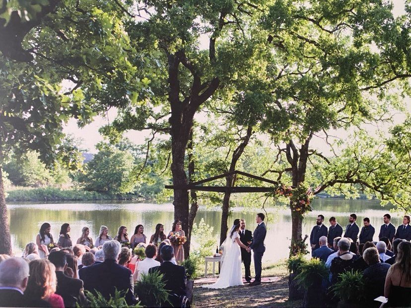 A bride and groom are getting married in front of a crowd of people in front of a lake.