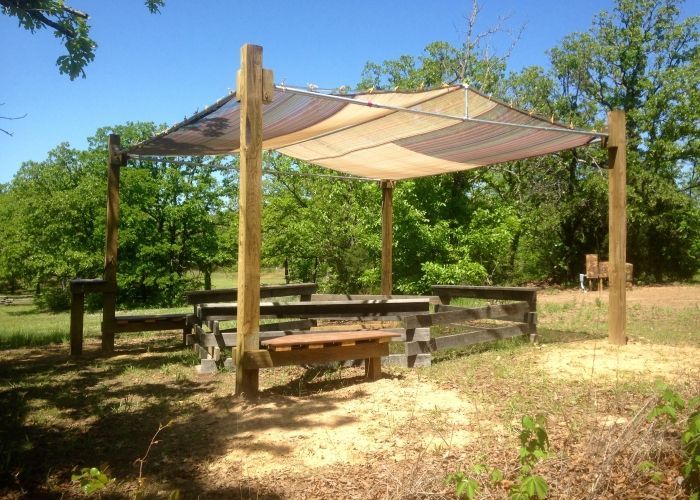 A picnic table under a canopy in a field with trees in the background.