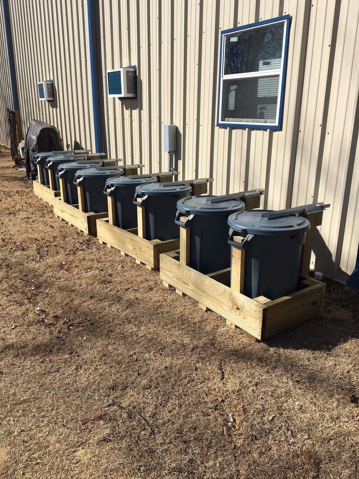 A row of trash cans are lined up in front of a building.