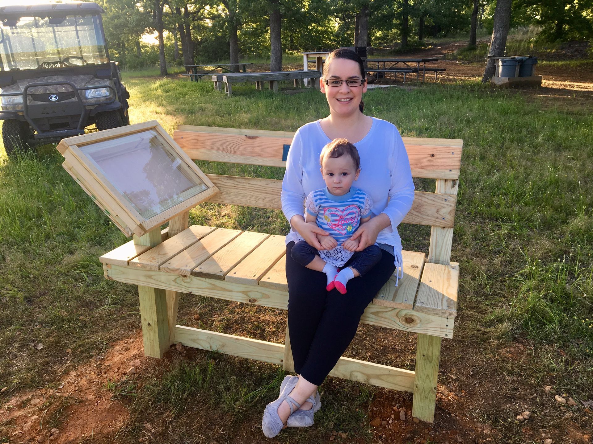 A woman is sitting on a wooden bench holding a baby.