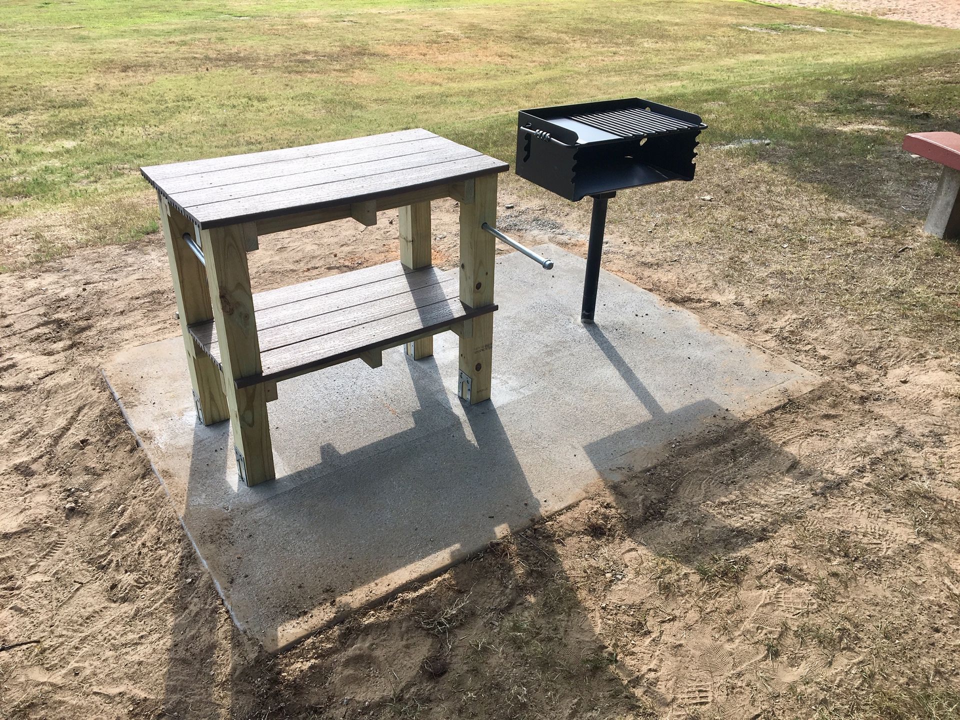 A wooden table is sitting next to a grill in a park.