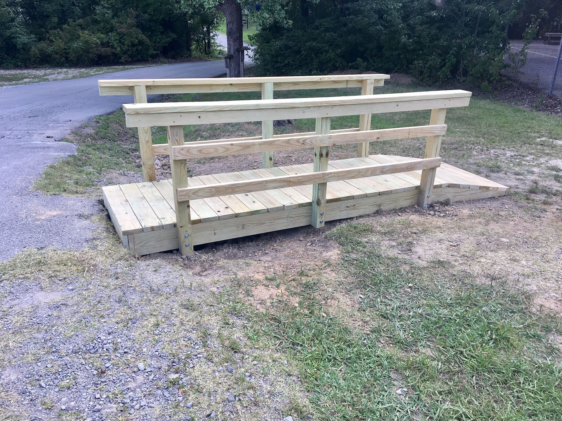 A wooden bridge is sitting in the grass next to a road.