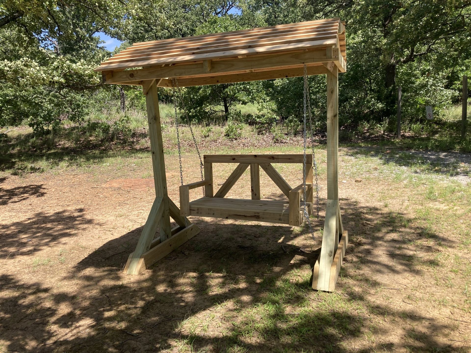 A wooden swing with a roof is sitting in the middle of a grassy field.