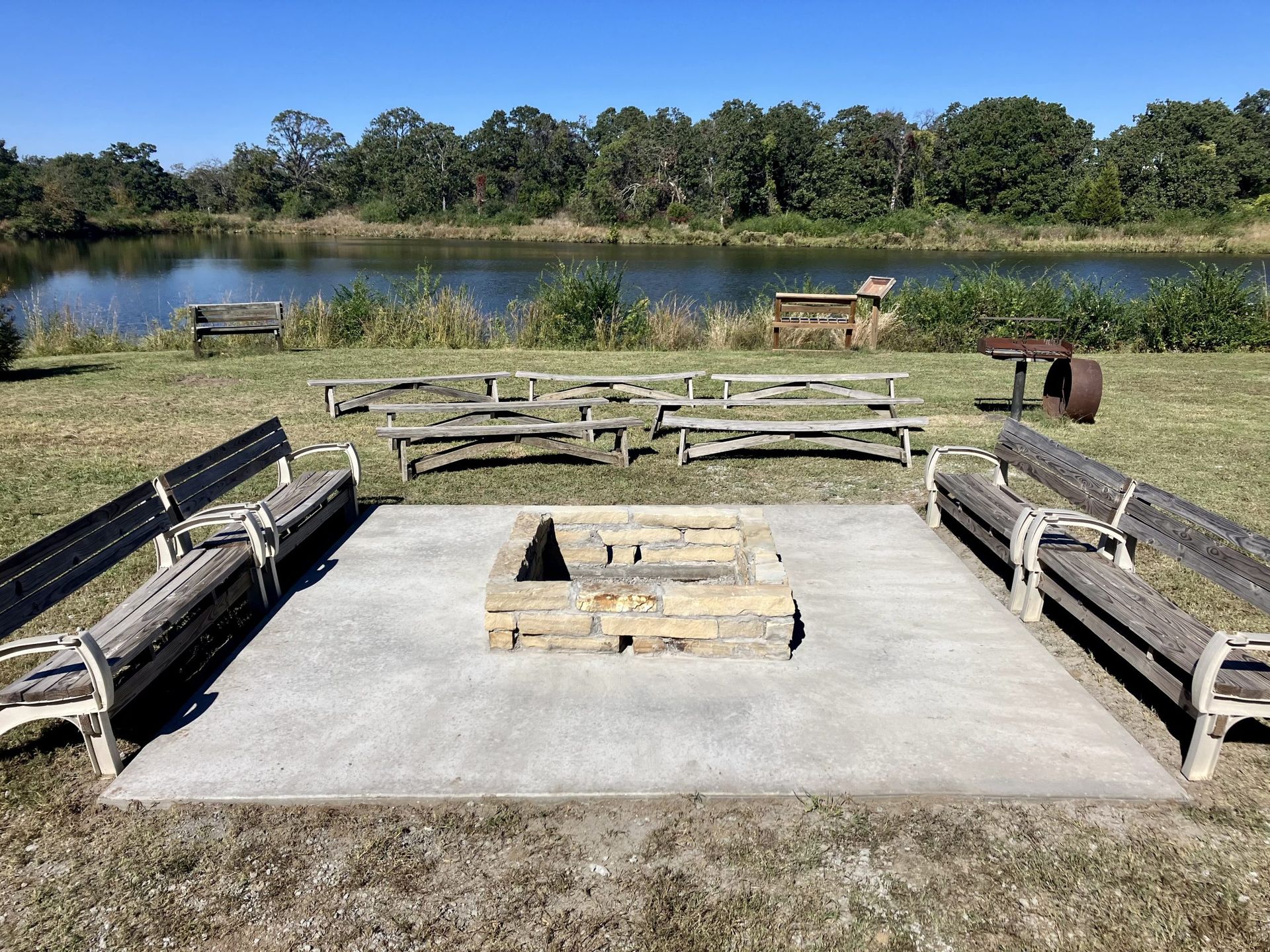 There is a fire pit in the middle of a field next to a lake.