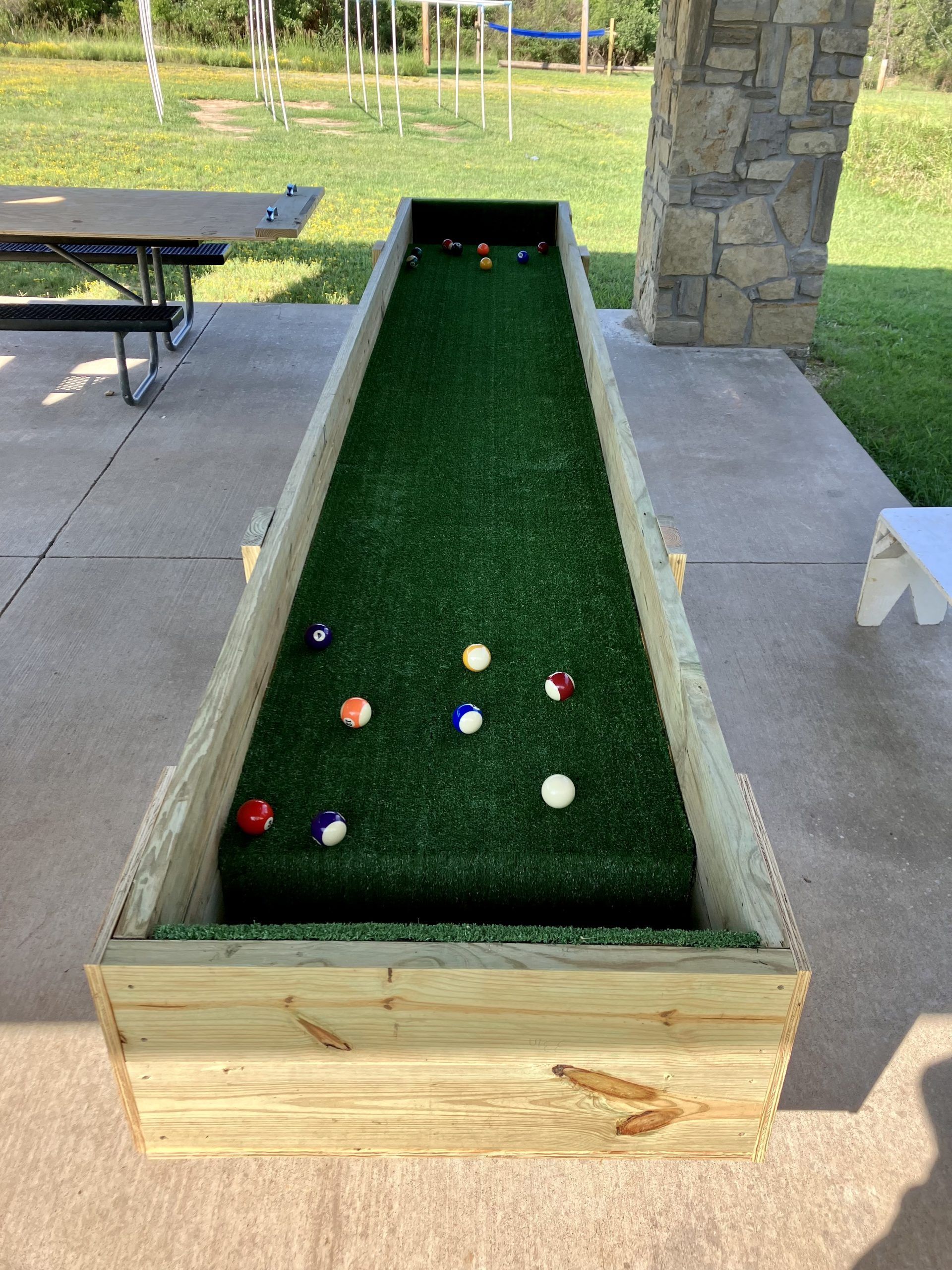 A wooden box filled with pool balls is sitting on a concrete patio.