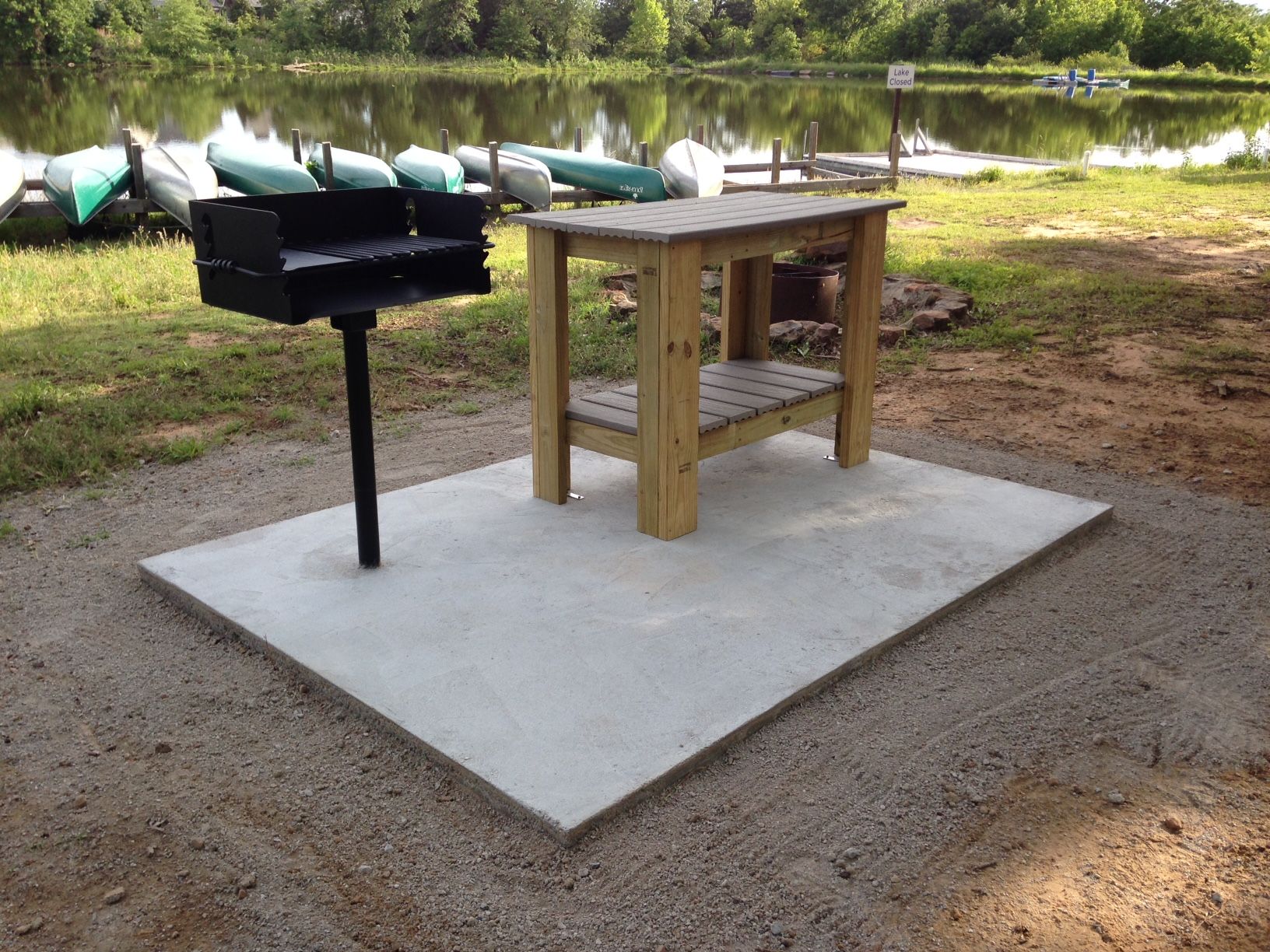 A wooden table with a grill next to a lake
