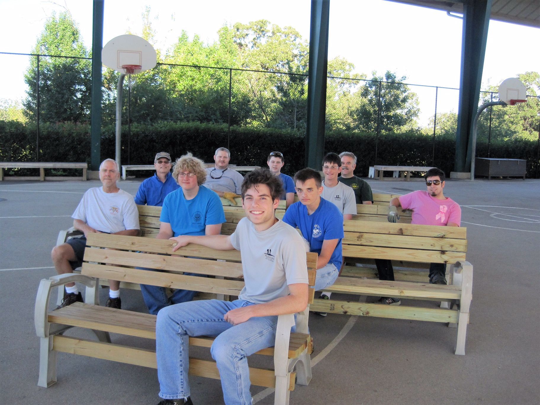 A group of young men are sitting on wooden benches in front of a basketball court