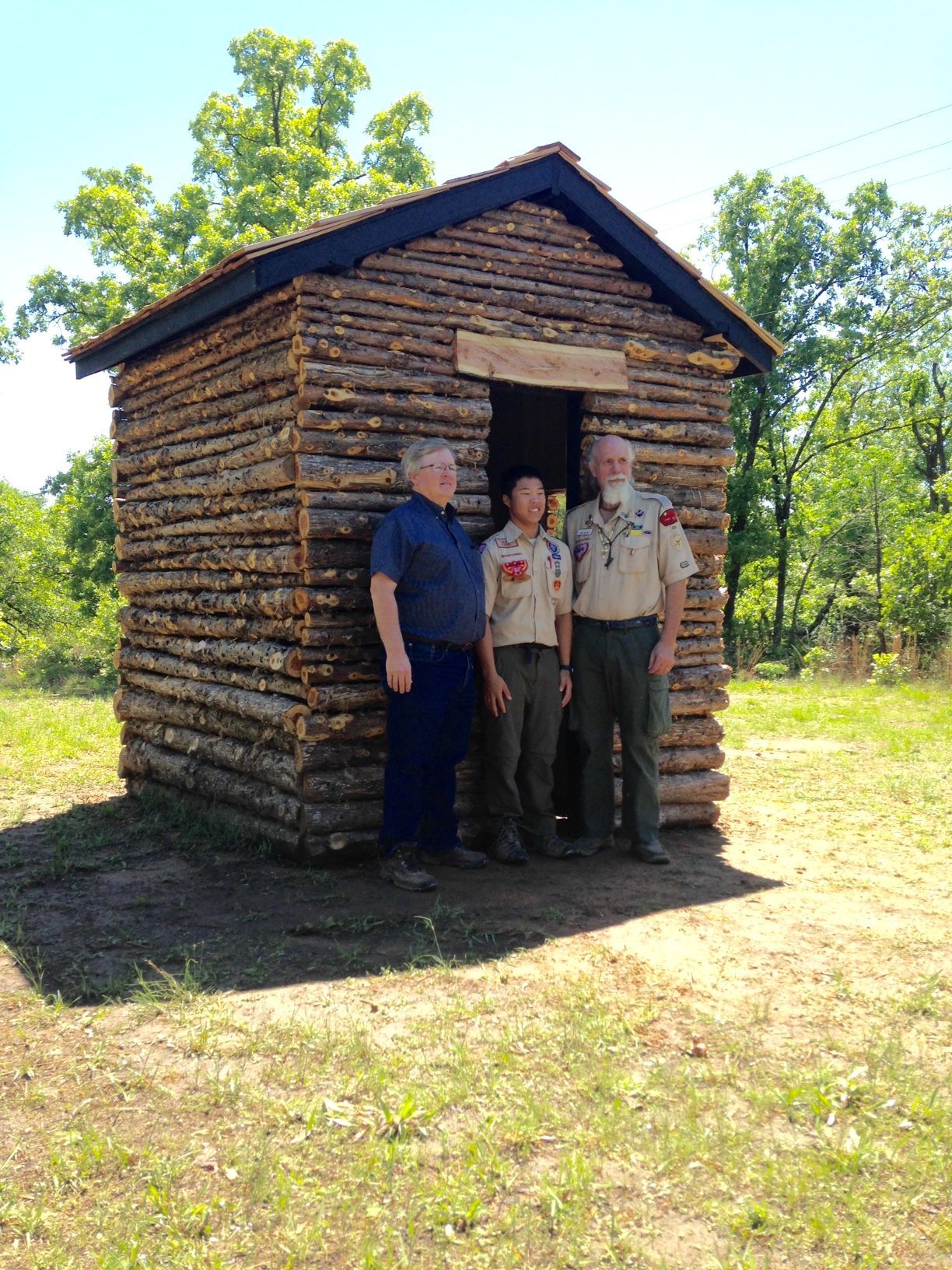 Three men are standing in front of a log cabin.