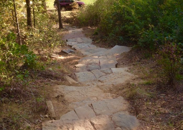 A stone path in the woods with a car parked on the side of it.