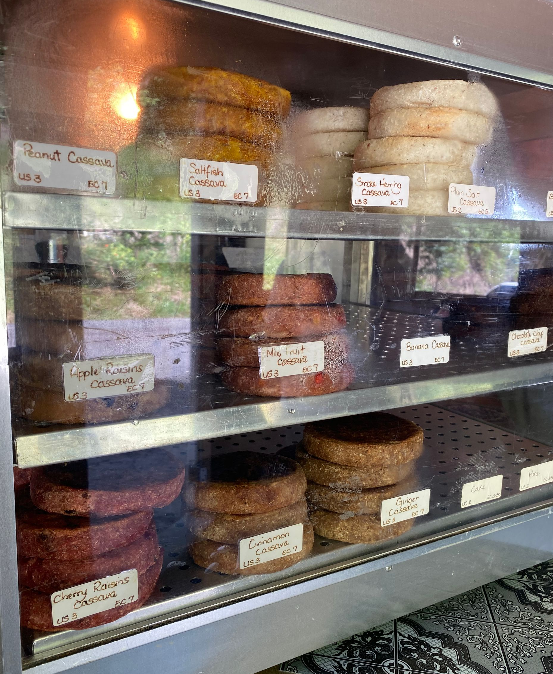 Glass case displaying stacked round baked goods with handwritten labels on shelves