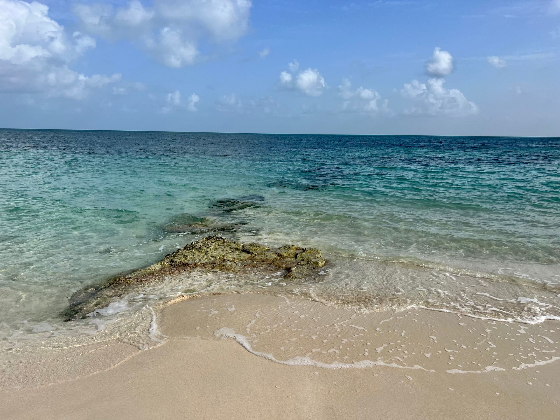 Sandy beach with clear turquoise waves and a rocky outcrop under a blue sky