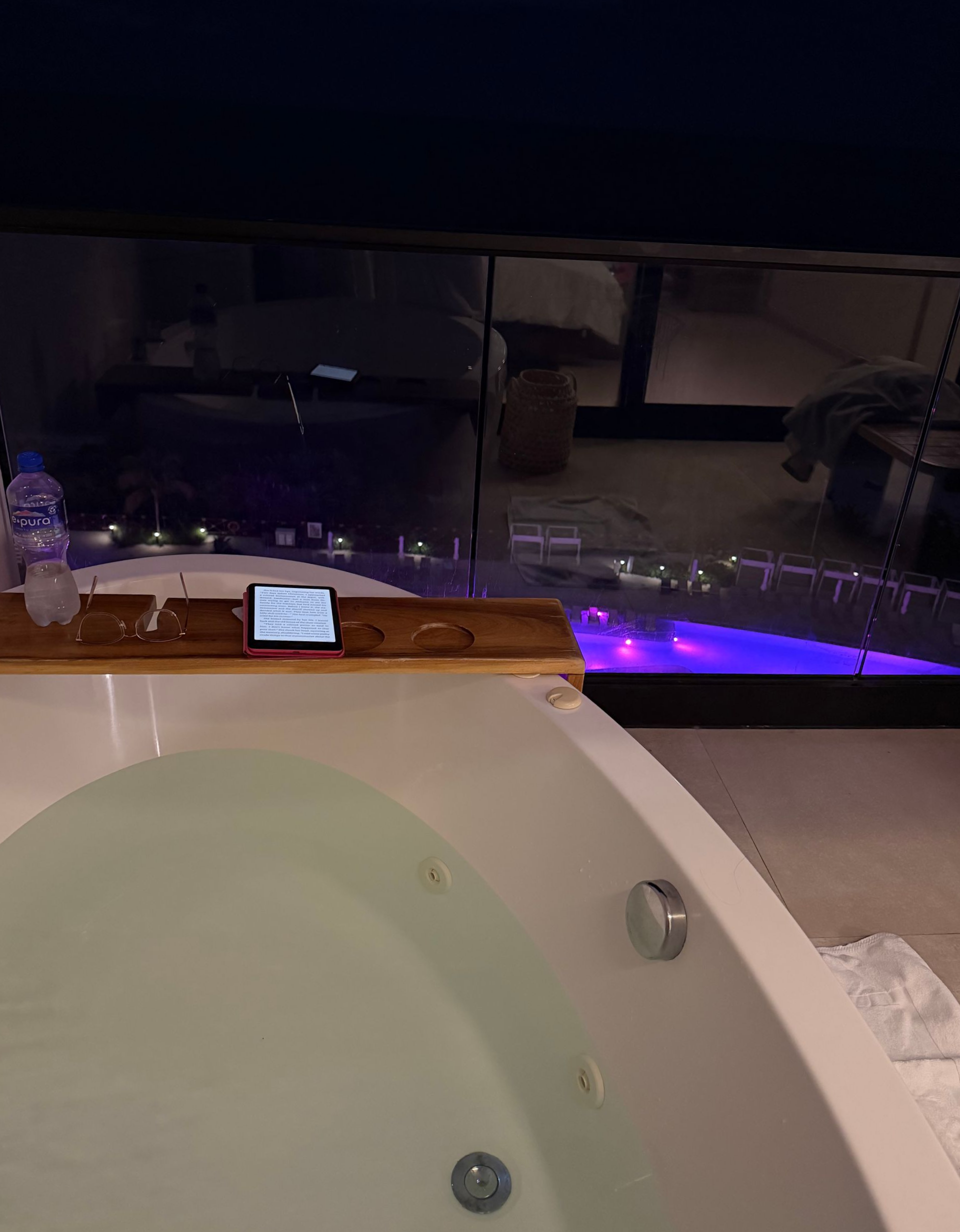 Legs in a hot tub facing a can on the edge, with blue-lit water and a dark wall backdrop