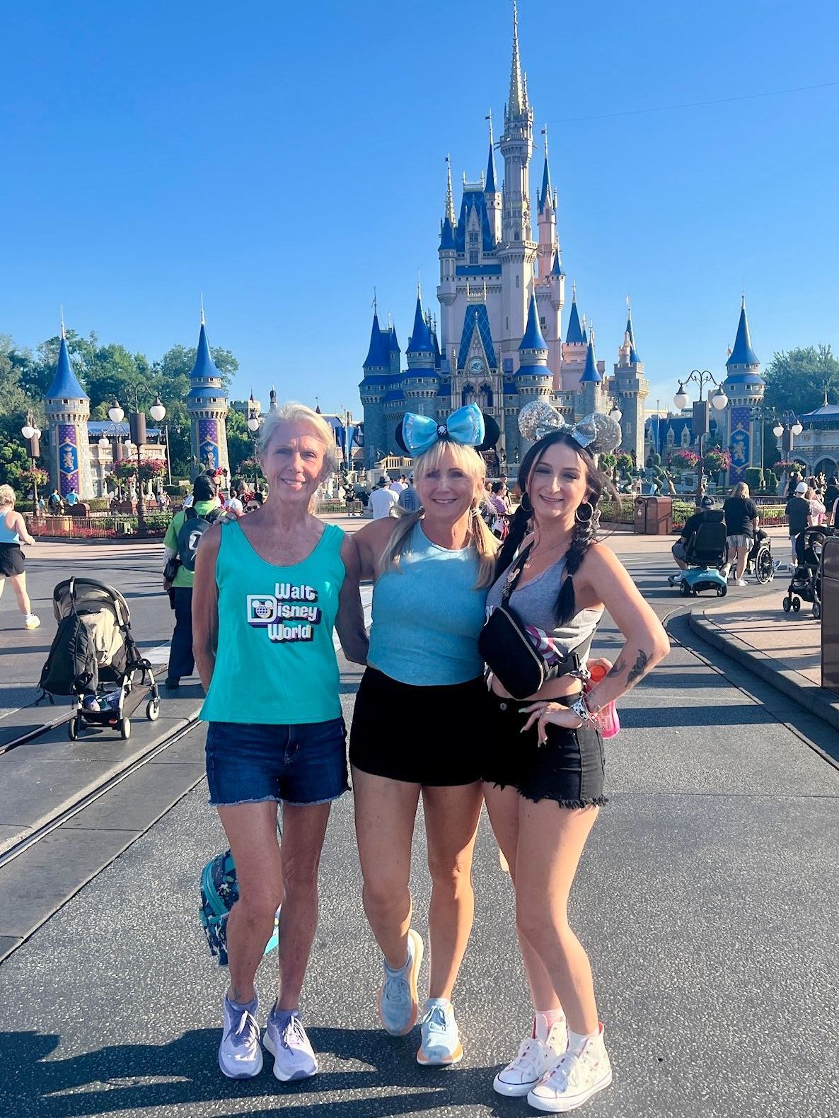 Three women pose in front of Cinderella's Castle at Disney World; sunny day.