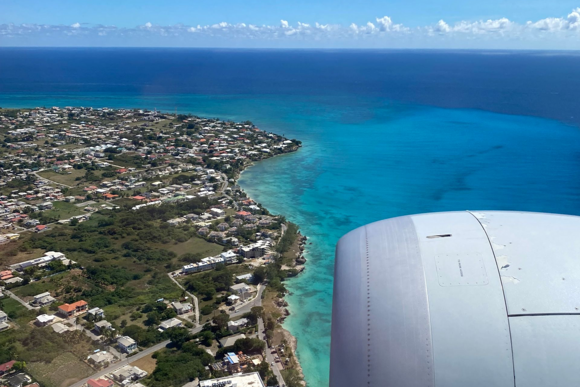 Aerial view of a coastal town beside turquoise ocean, seen from an airplane window with engine visible