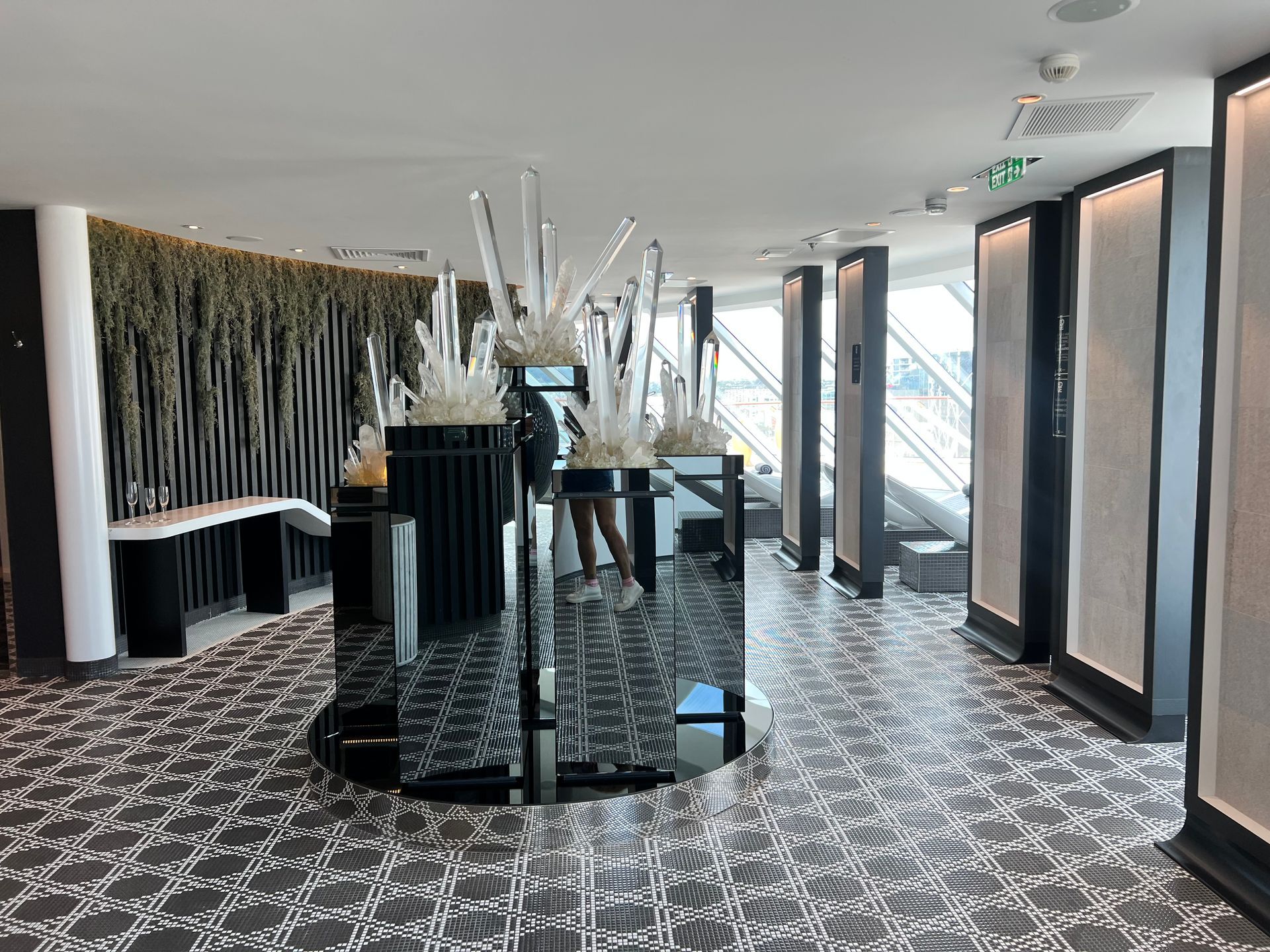 Modern cruise ship spa with patterned carpet, glass tables, and tall windows overlooking a bright day