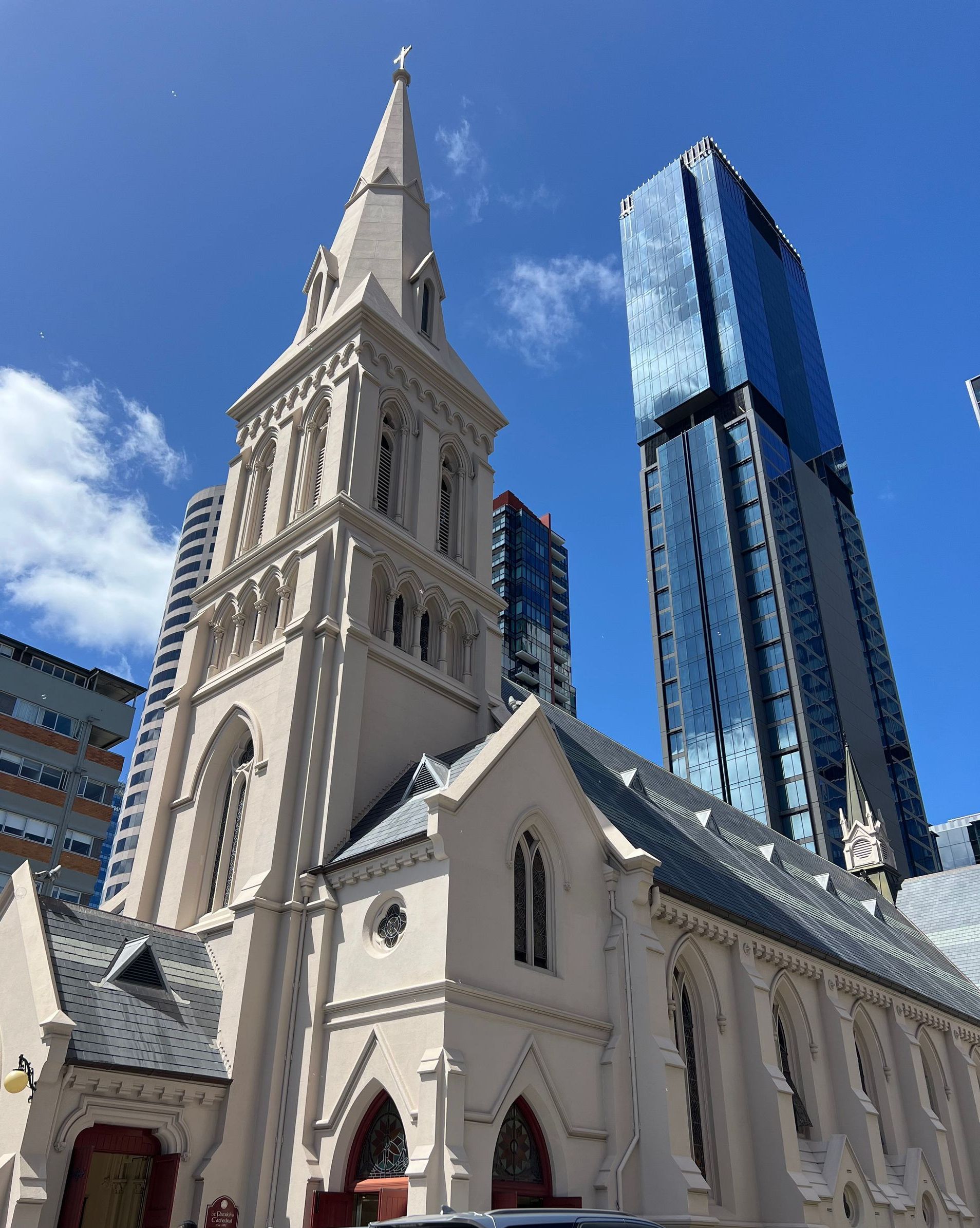 Gothic church with tall spire and modern glass skyscraper against a blue sky. Auckland, New Zealand