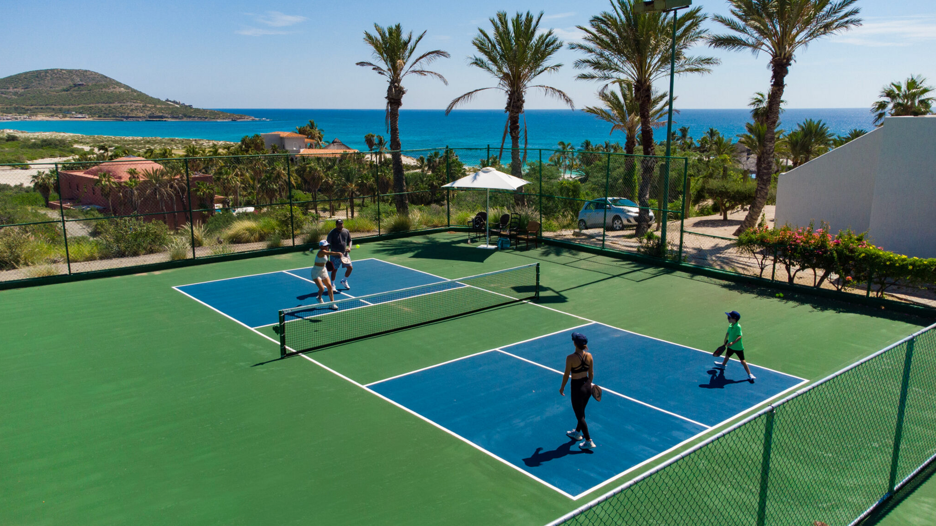 People playing pickleball on bright blue courts by a tropical seaside resort