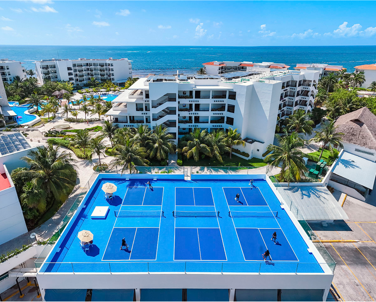 Rooftop pickleball courts on a seaside resort with palm trees and ocean view
