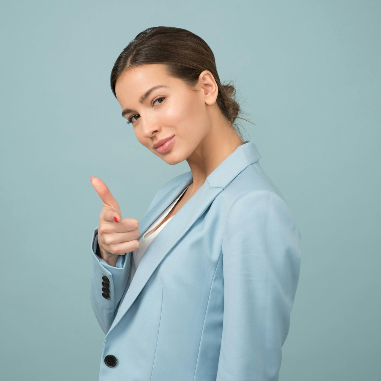 Woman in a blue blazer points at the viewer with a confident expression; light blue background.
