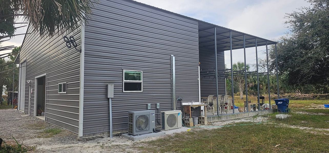 Gray metal building with a covered porch; air conditioning units are in front.