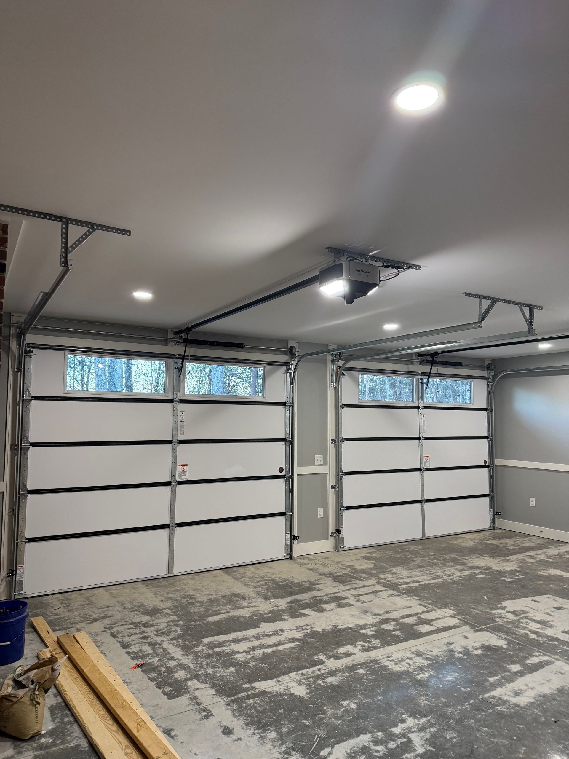 Empty garage with two white doors, gray floor, and overhead lights