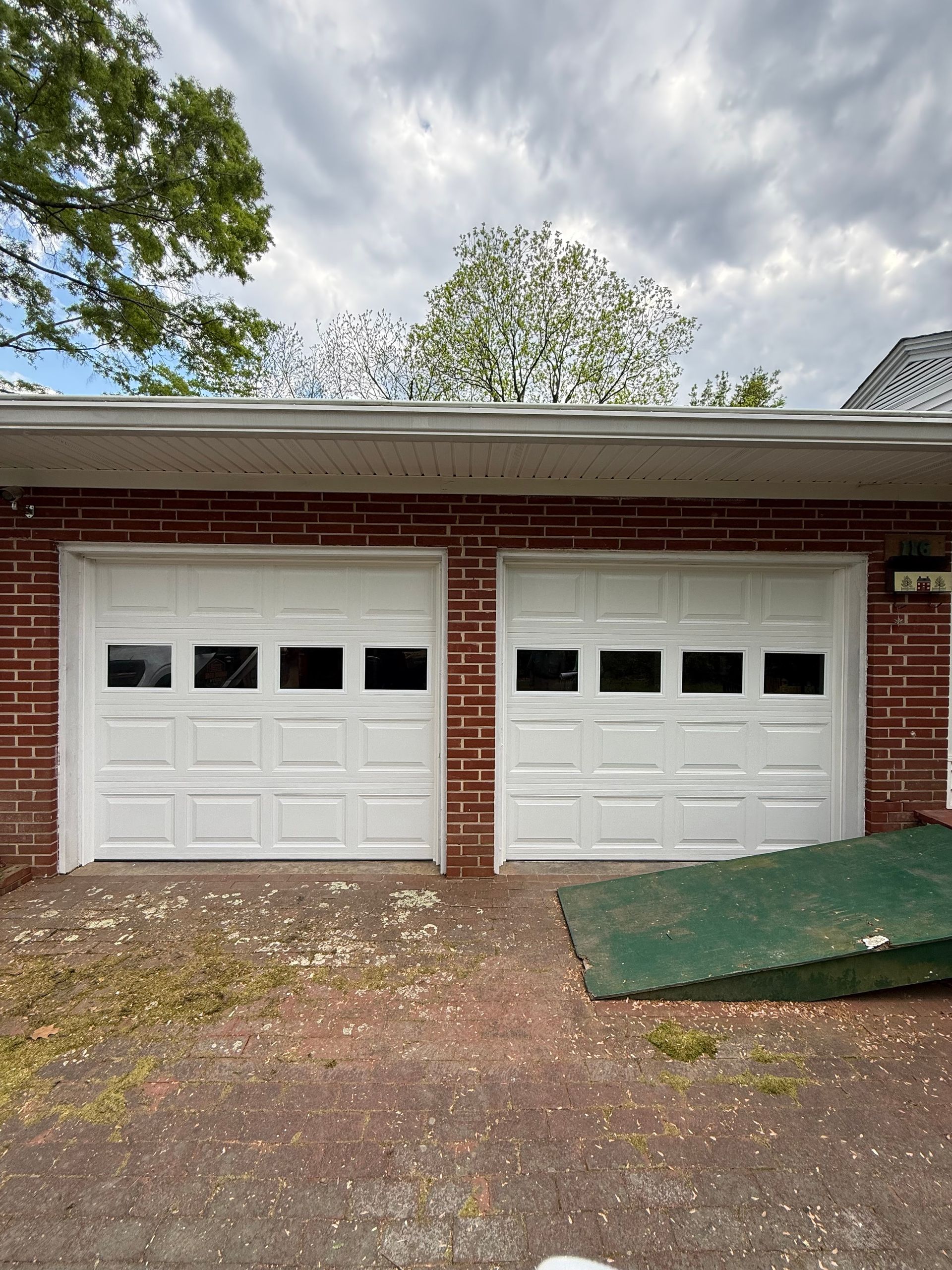 Two white garage doors on a red brick house with a driveway and cloudy sky