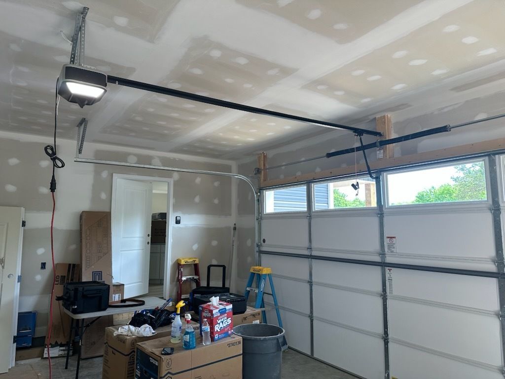 Garage interior under renovation with drywall, tools, and an open garage door.