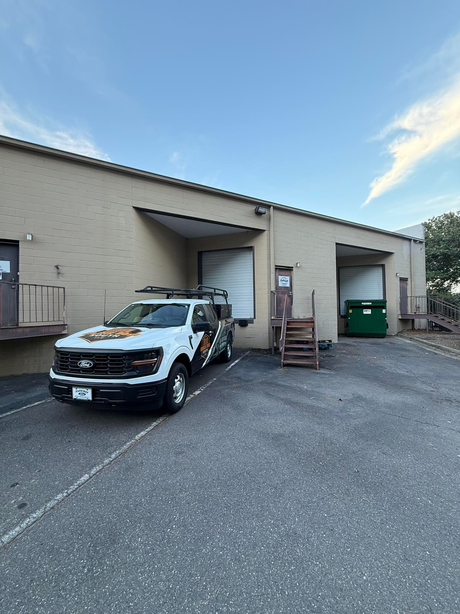 Truck parked outside warehouse loading bays under a blue sky