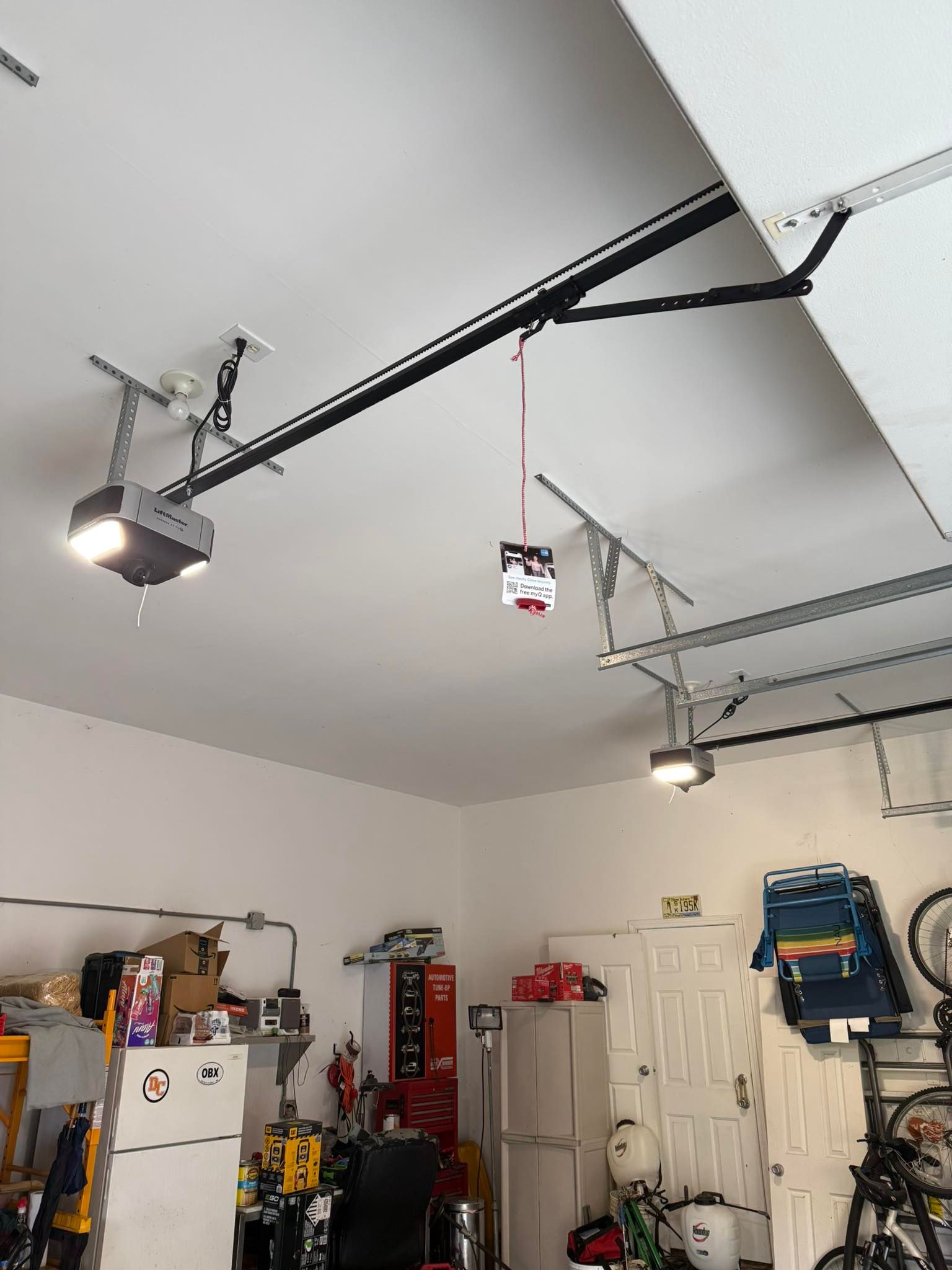 Garage interior with ceiling track lights, storage shelves, tools, and a hanging work light.
