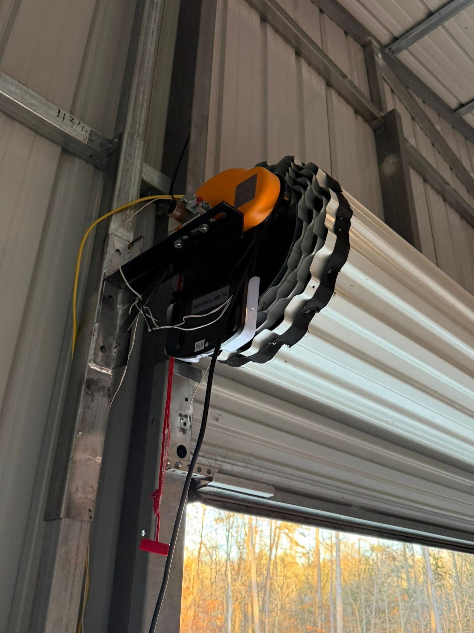 Black-and-orange garage door opener mounted on a metal beam near a raised garage door