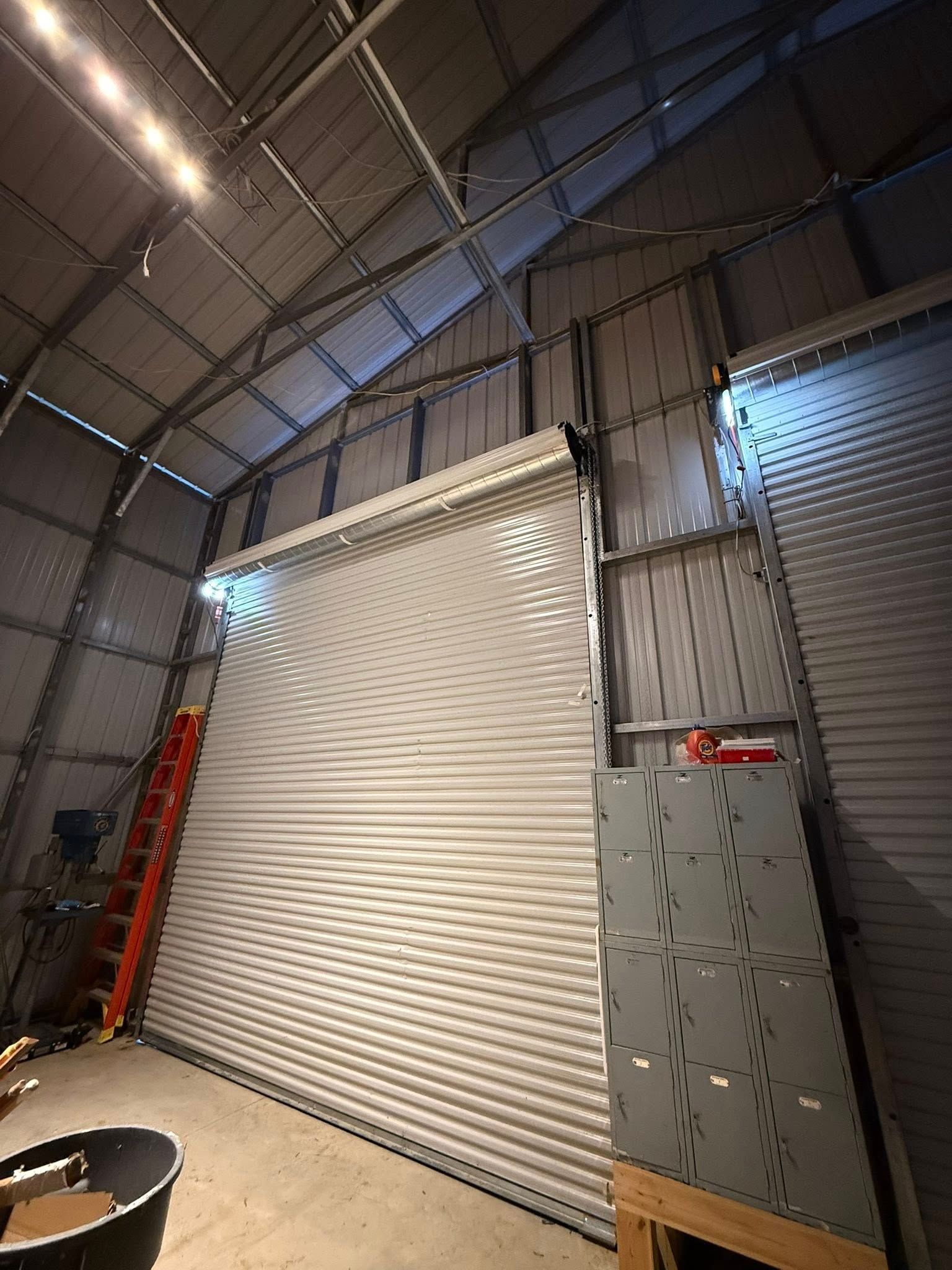 Industrial warehouse interior with a large white roll-up door and metal wall panels under high arched ceiling.