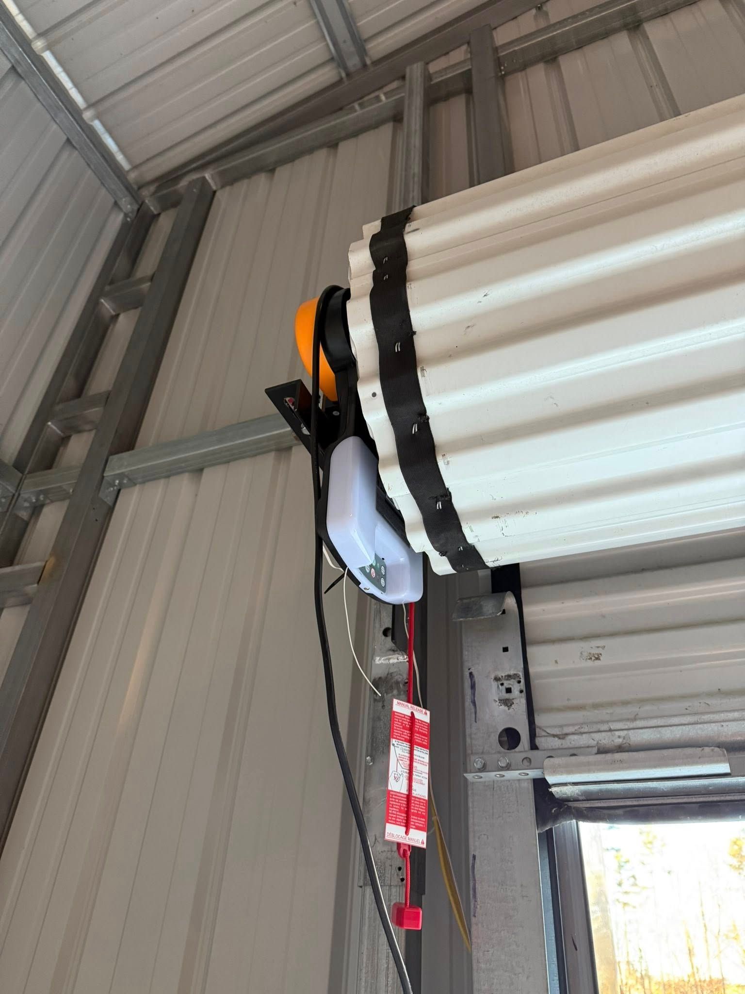 Industrial ceiling-mounted light with black strap and orange housing in a metal warehouse interior