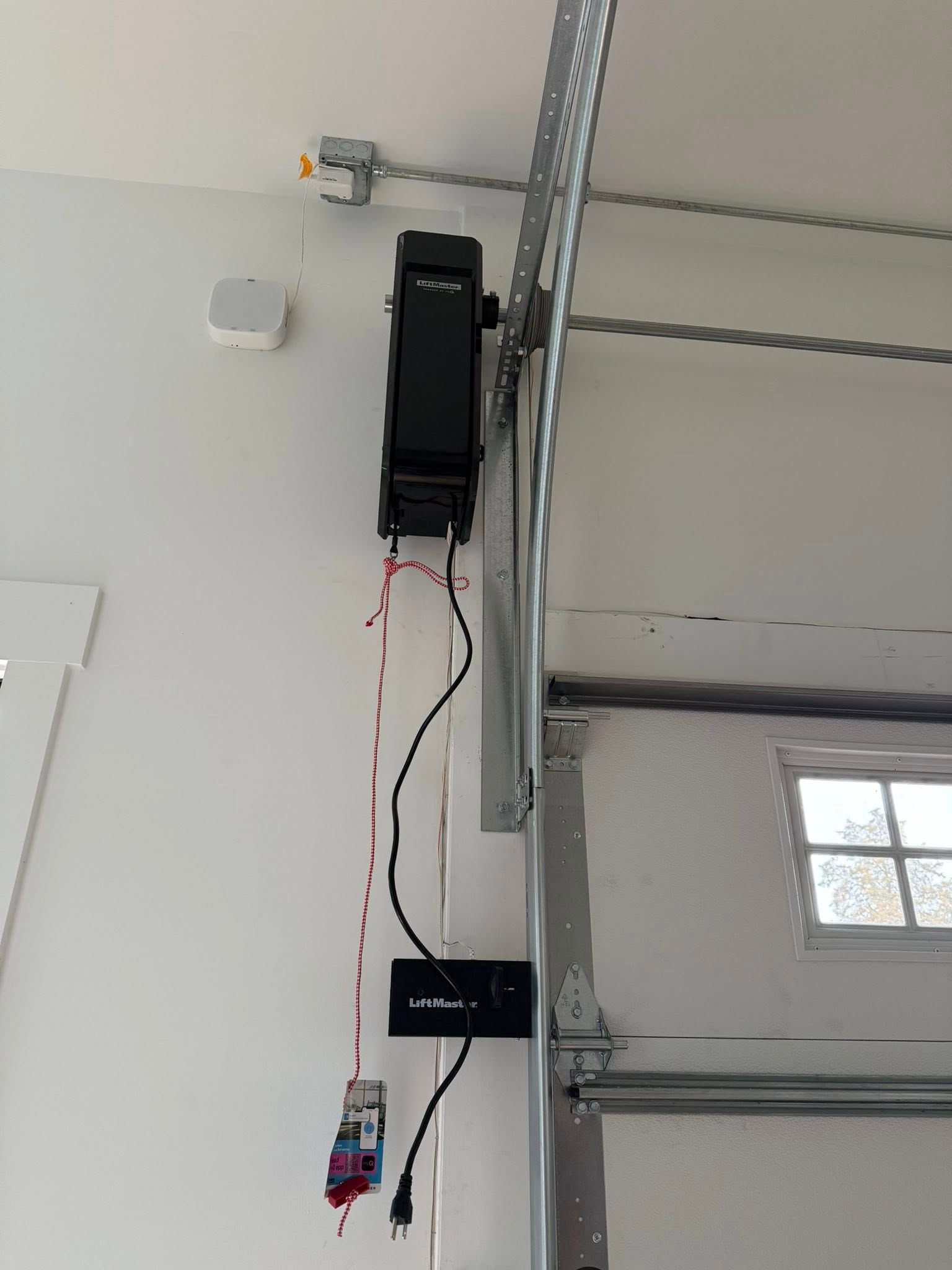 Garage wall-mounted device with hanging red and black wires beside a garage door track