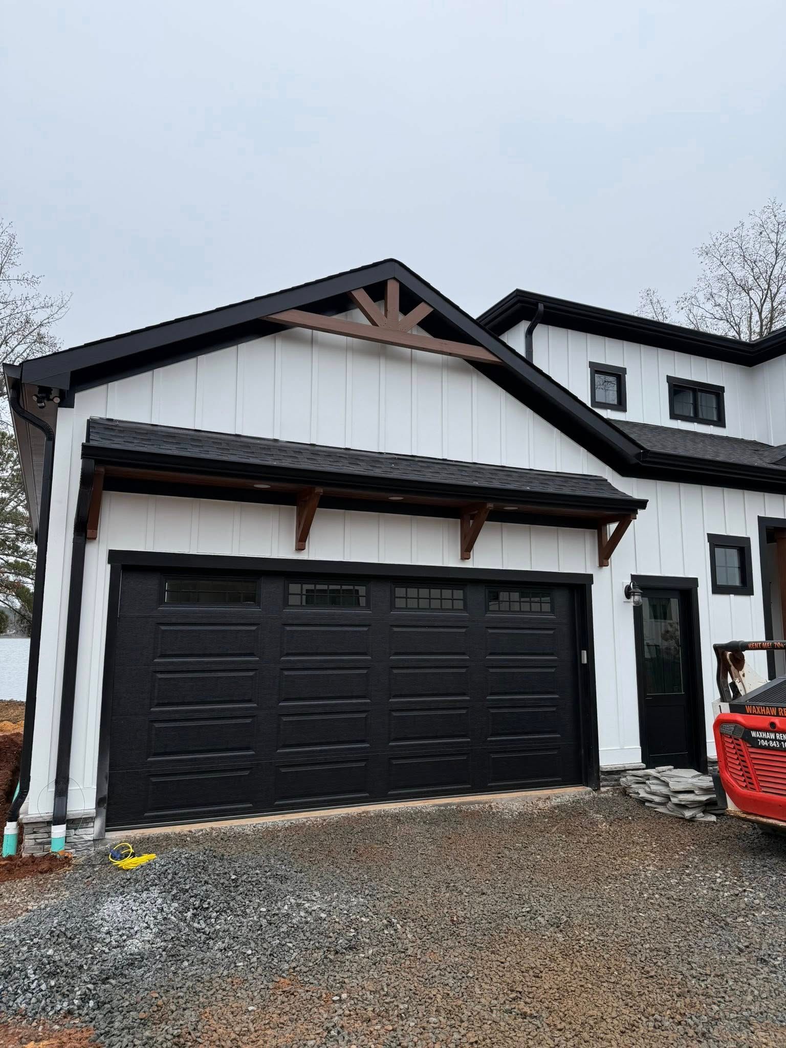 White two-story house with black garage door and red truck on a gravel driveway