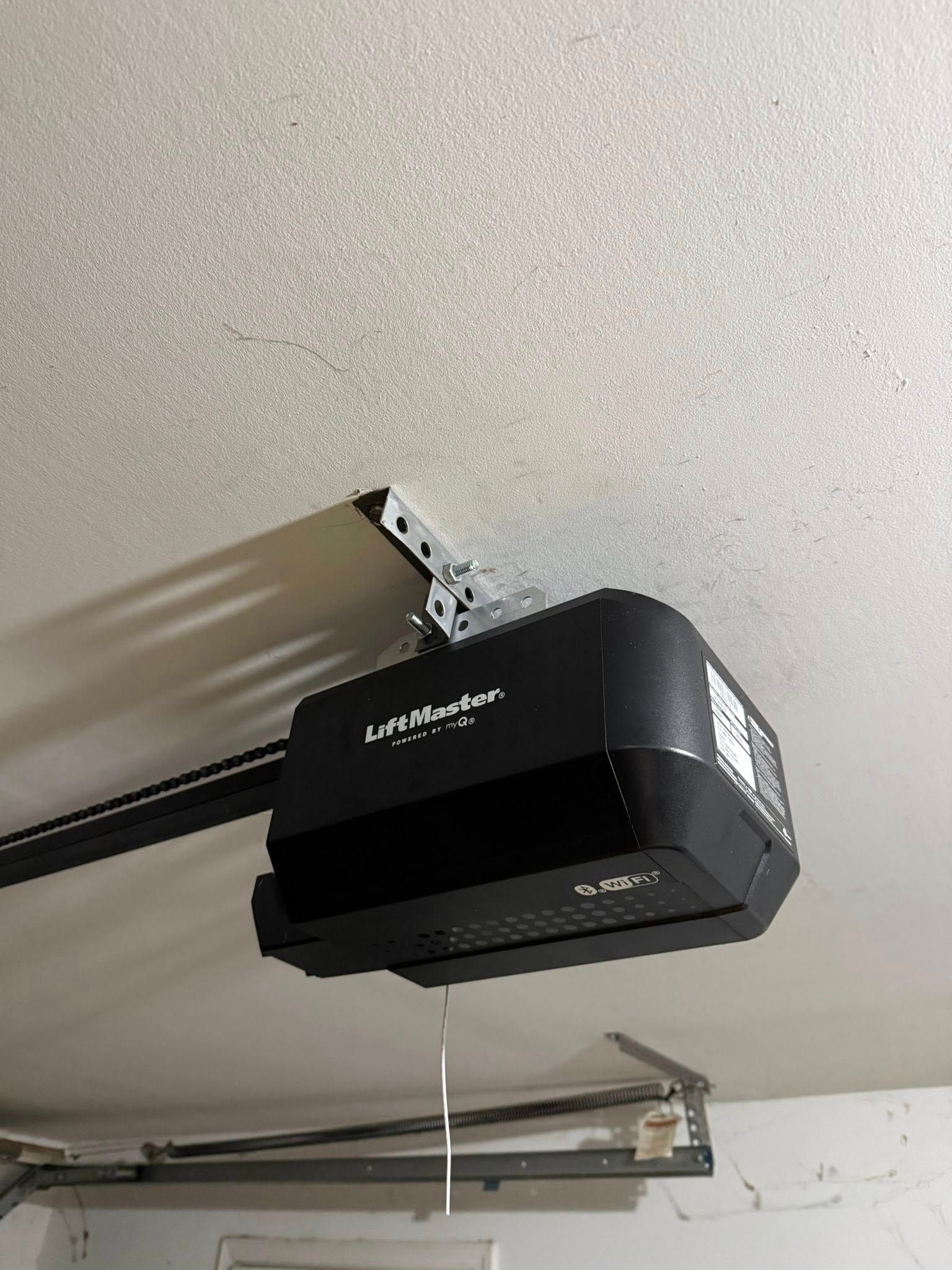 Ceiling-mounted garage door opener with hanging pull cord and metal track.