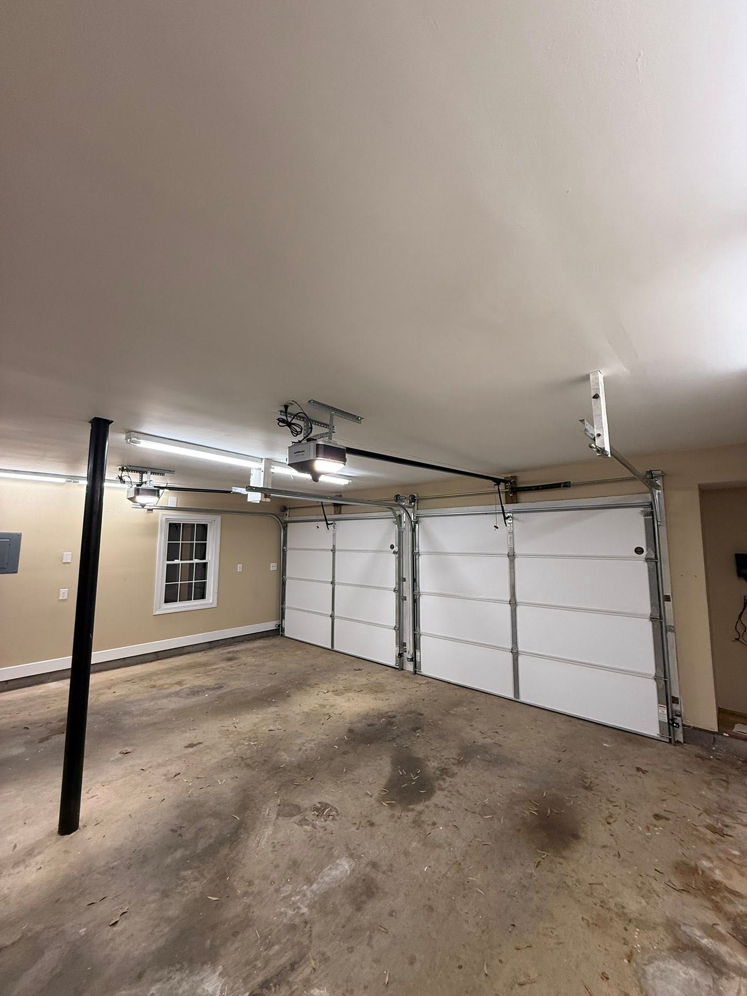 Empty garage interior with white double doors, concrete floor, and overhead opener lights