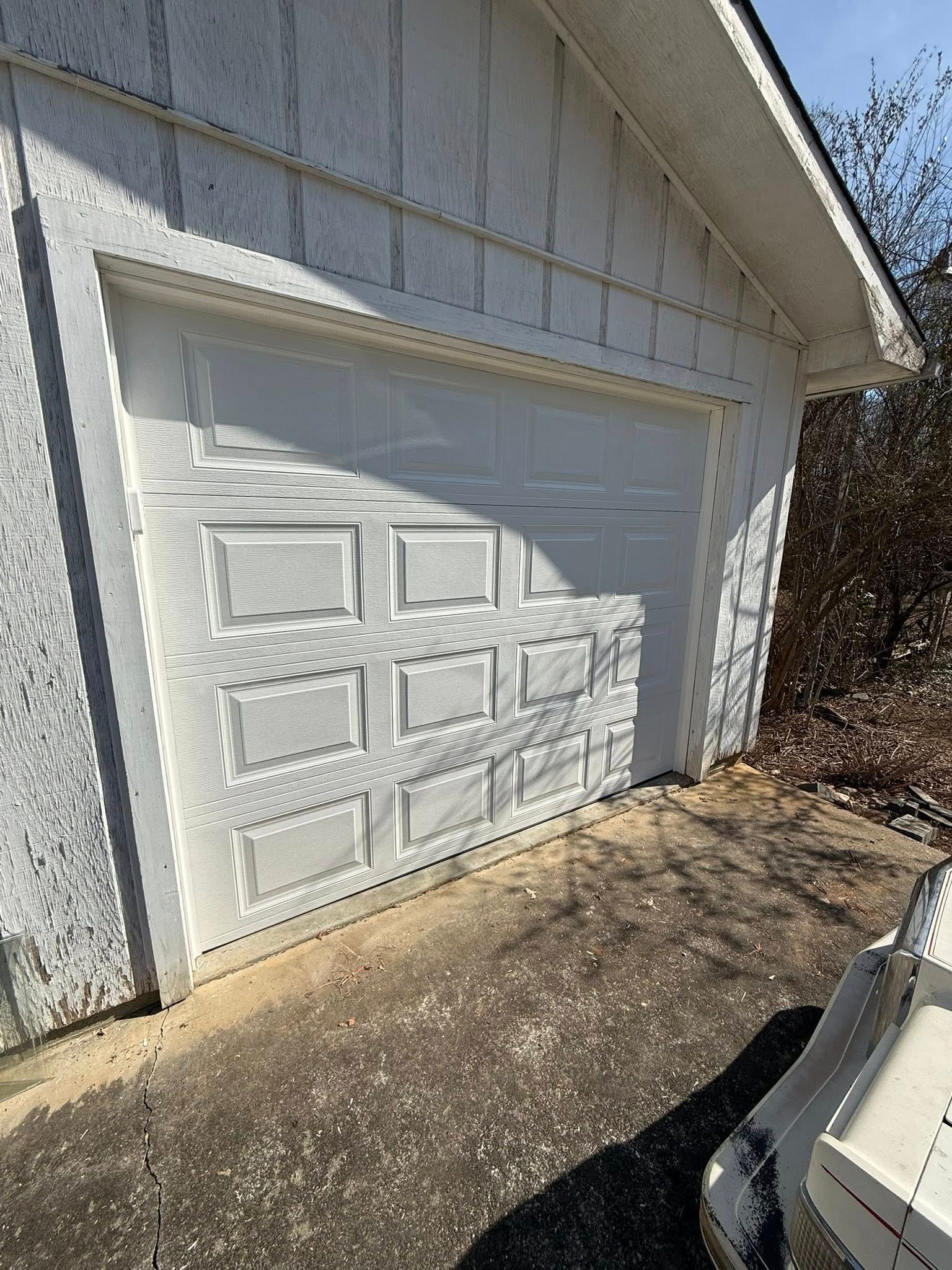 White garage door on a detached garage with peeling paint and a concrete driveway in sunlight