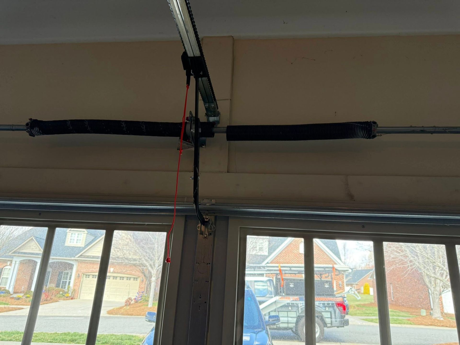 Garage door opener mounted above windows with hanging cables and a red cord