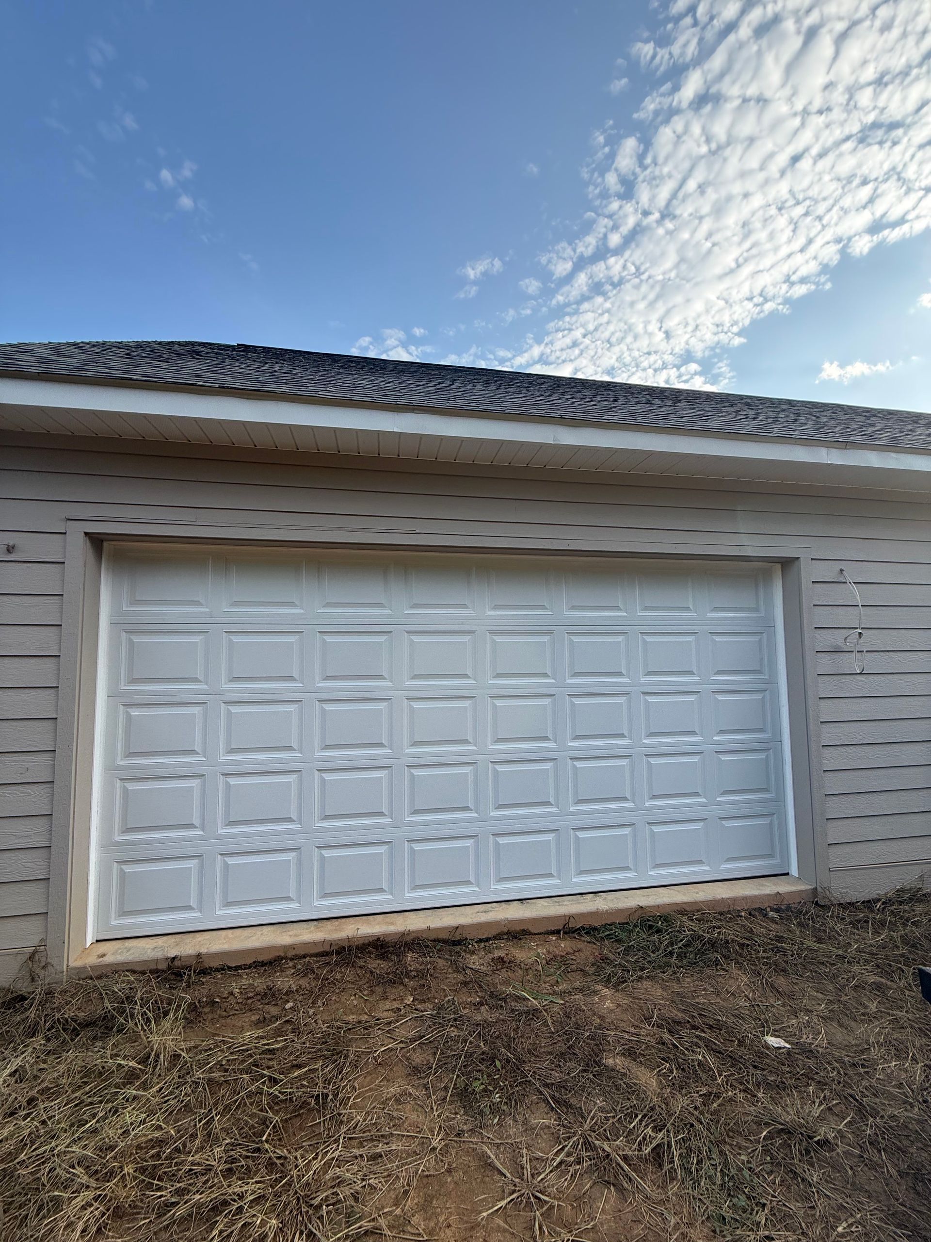 Two white garage doors beneath a dark shingled roof on a concrete driveway