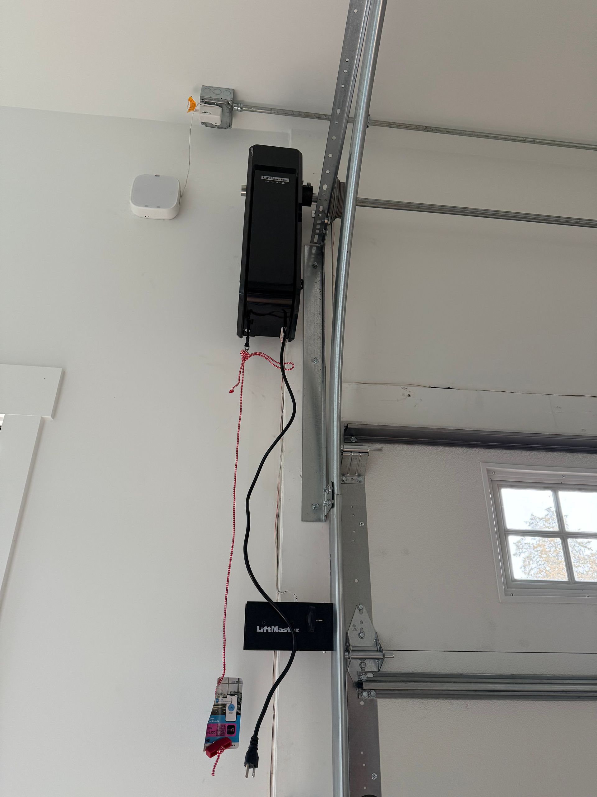 Technician adjusting a ceiling-mounted garage door opener with a step ladder below